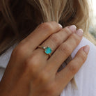 A model's hand wearing a sterling silver round, small, claw-set dichroic glass gem ring in turquoise tones.