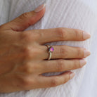 Model wearing a sterling silver round, small, claw-set dichroic glass gem ring in pink tones.