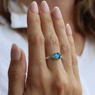 A model's hand wearing a sterling silver round, small, claw-set dichroic glass gem ring in blue tones.
