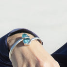 Silver bracelet with revalued bombay sapphire glass gem on a person's wrist against a neutral background