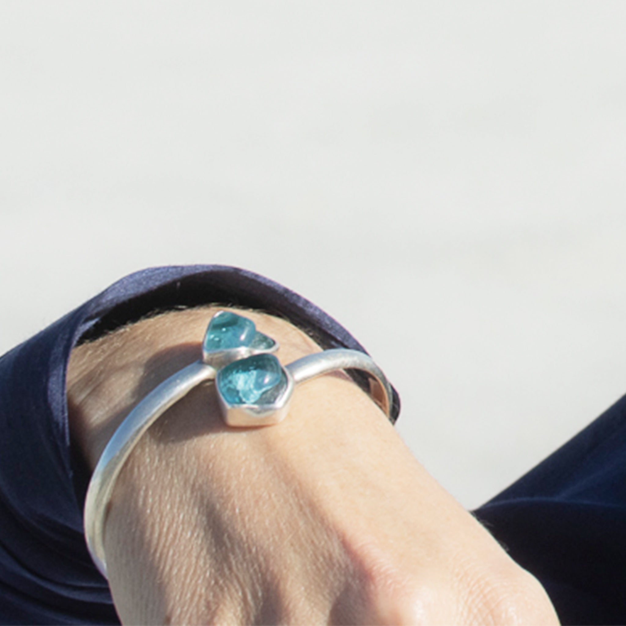 Silver bracelet with revalued bombay sapphire glass gem on a person's wrist against a neutral background