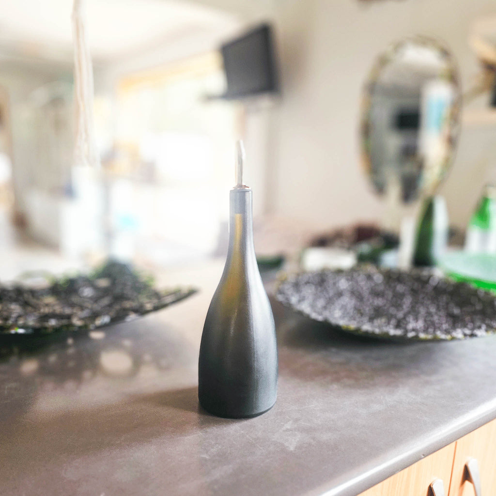 •	Image of the Prestige Glass Oil Pourer This unique and luxurious accessory, born from upcycled champagne bottles, elevates your kitchen with its one-of-a-kind matte sateen finish and heat-altered shape.